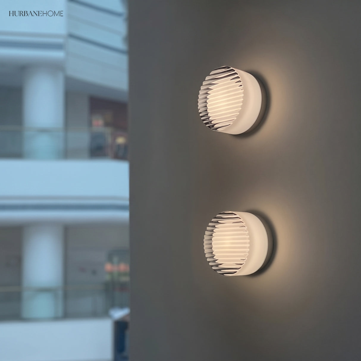 Two ribbed round wall lights on an exterior wall beside glazing