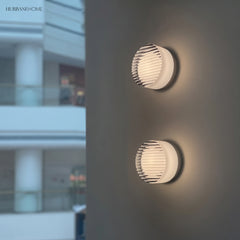 Two ribbed round wall lights on an exterior wall beside glazing