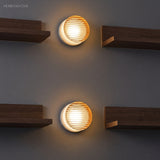 Two ribbed wall lights on a dark wall between walnut shelves