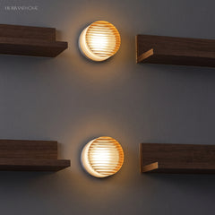 Two ribbed wall lights on a dark wall between walnut shelves