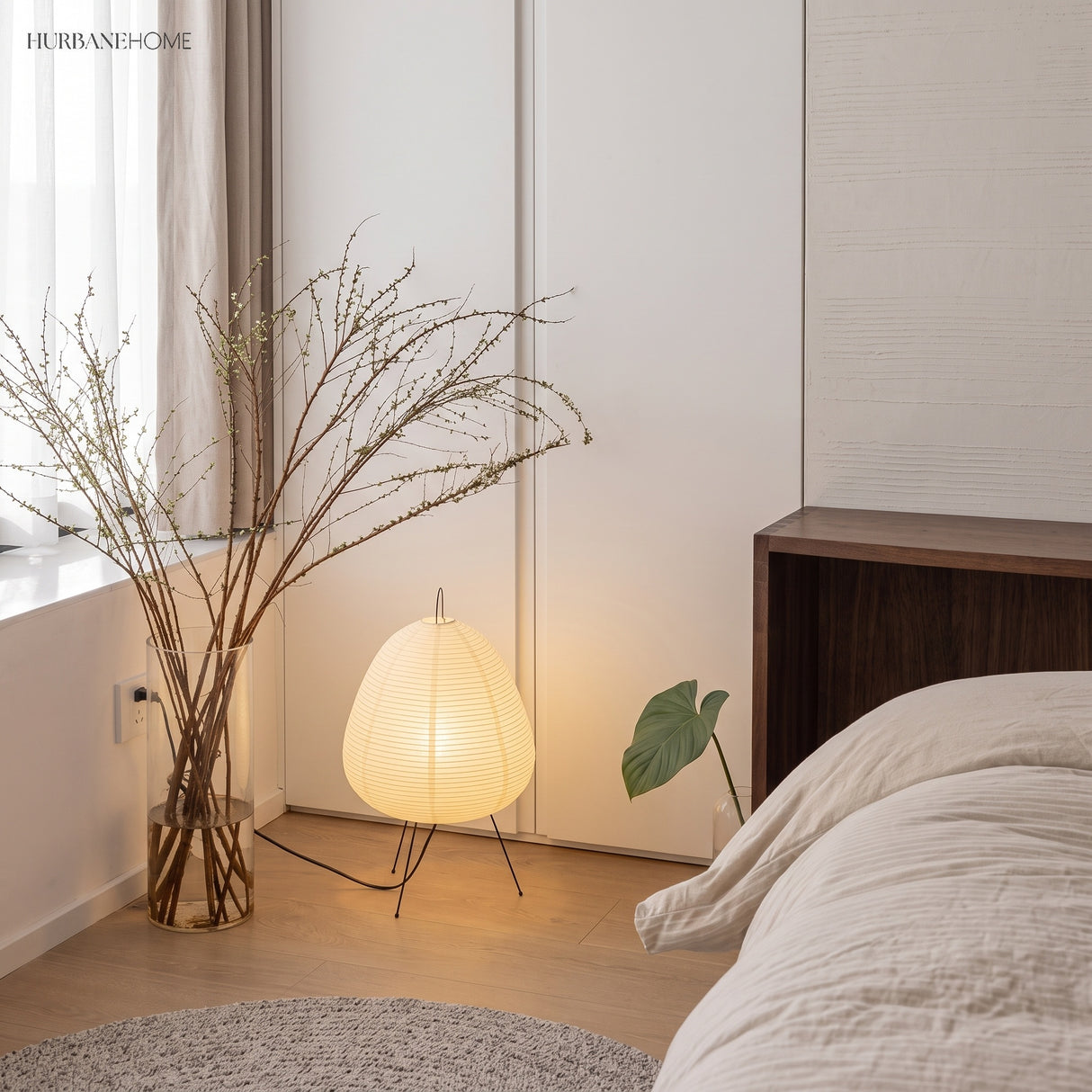 Rice paper table lamp glowing in a bedroom corner beside dried branches