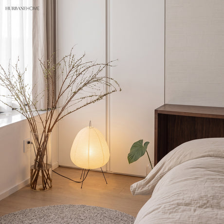 Rice paper table lamp glowing in a bedroom corner beside dried branches
