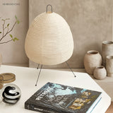 Rice paper table lamp on a white desk beside ceramic vessels