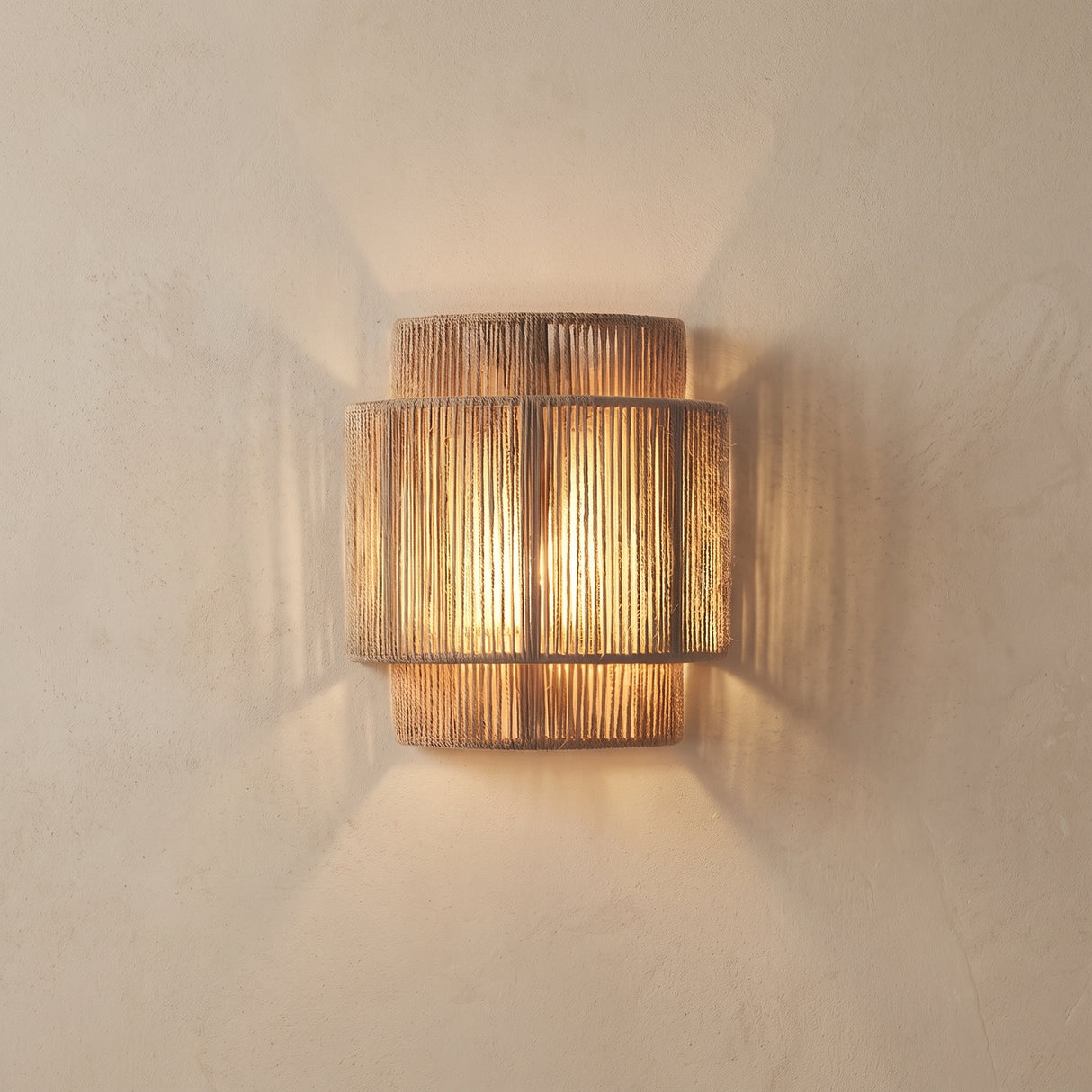 Woven rope wall lamp lit against a plain plaster wall