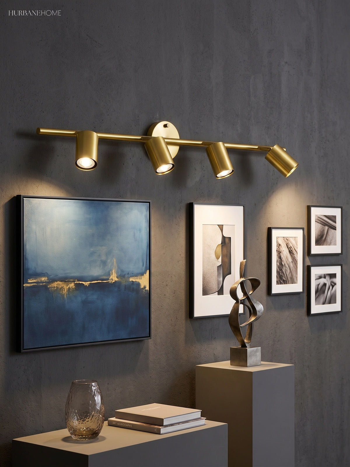 Brass spotlight bar lit on a dark wall above framed pictures and a sculpture