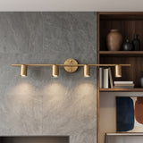 Brass four head spotlight bar lit on a grey stone wall beside timber shelving