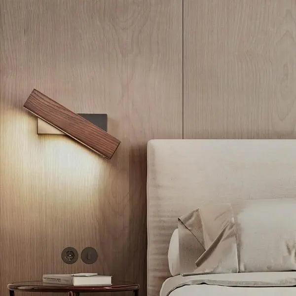 Walnut bar sconce lit above a bed with a pale upholstered headboard