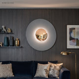 Grey disc wall sconce with a gold centre lit above a blue sofa