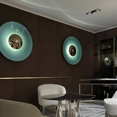 Two disc sconces in blue and green lit in a dark dining room