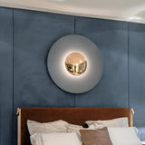 Grey disc sconce with a chrome centre lit above a blue headboard