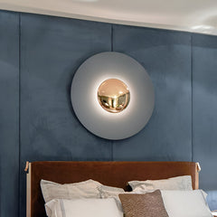 Grey disc sconce with a chrome centre lit above a blue headboard