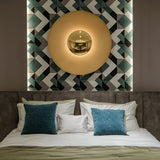 Gold disc sconce lit above a bed with a patterned wall panel