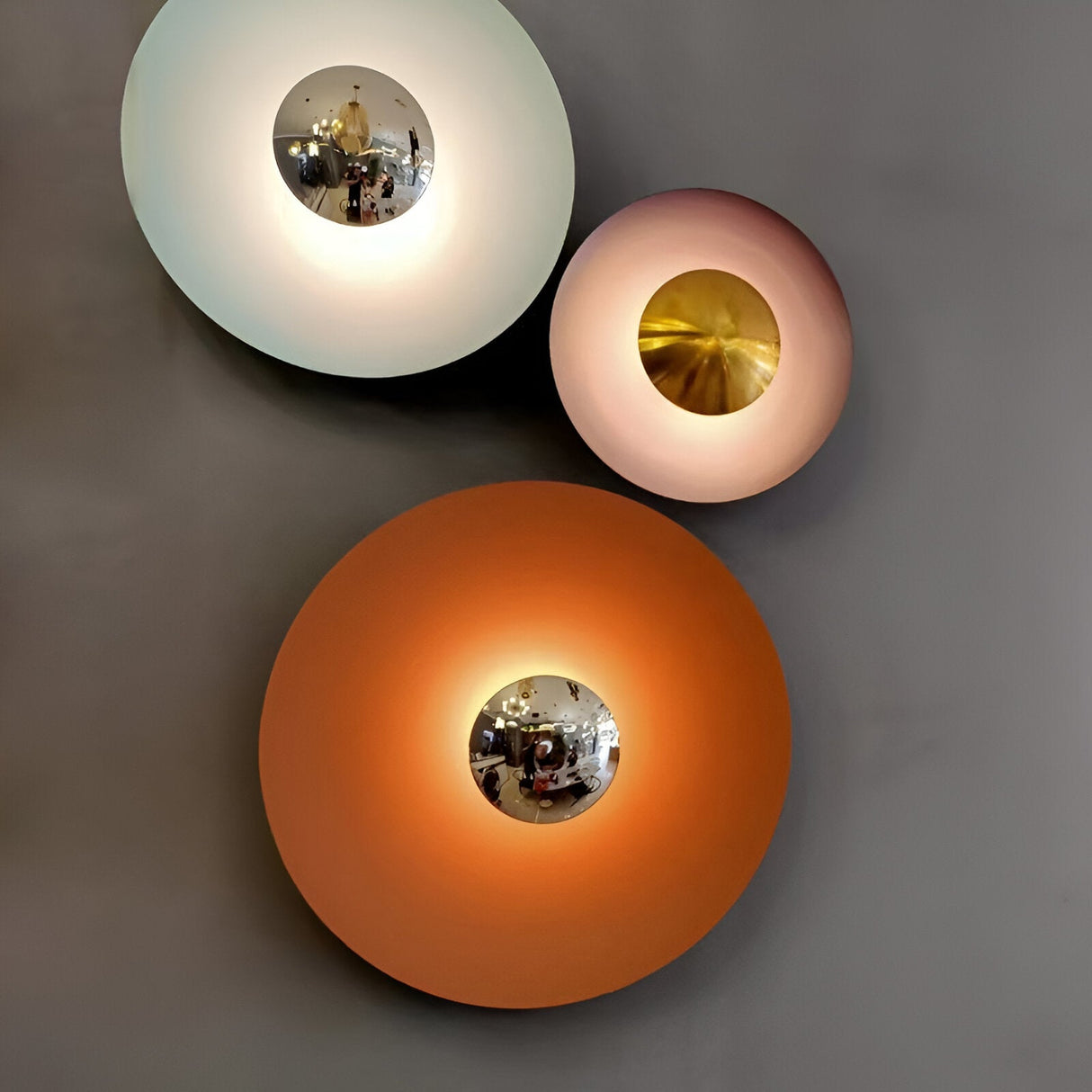 Three disc sconces in white pink and orange grouped on a wall