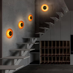 Four orange disc sconces lit along a wall beside a staircase