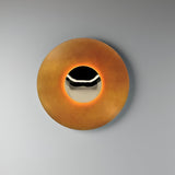 Light orange disc sconce lit on a pale grey wall