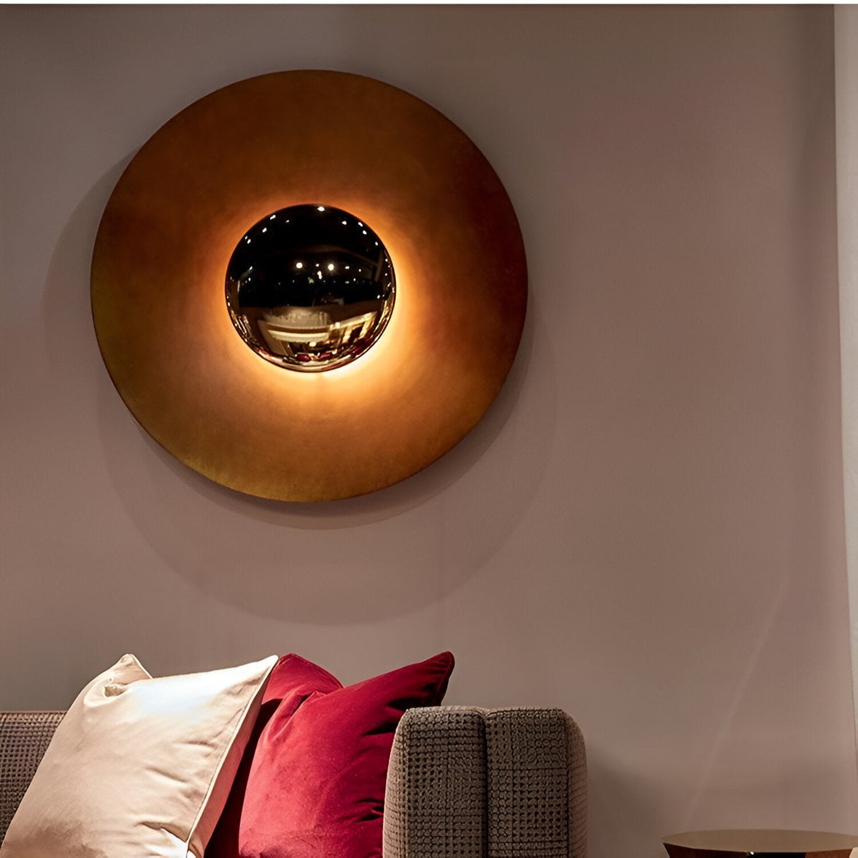 Large orange disc sconce lit on a pink wall above a sofa