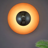Orange disc sconce lit on a grey wall showing the glow ring