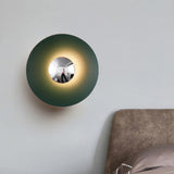 Green disc sconce lit on a white wall beside an armchair