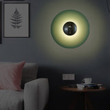 Green disc sconce lit on a grey wall beside a framed fern print
