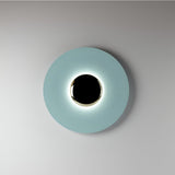 Blue disc sconce with a black centre lit on a pale wall