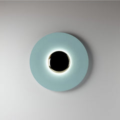 Blue disc sconce with a black centre lit on a pale wall
