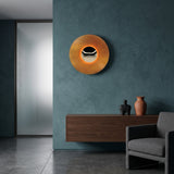 Orange disc wall sconce with a chrome centre lit on a teal wall