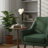 Sage green flower table lamp lit on a side table beside a green velvet armchair
