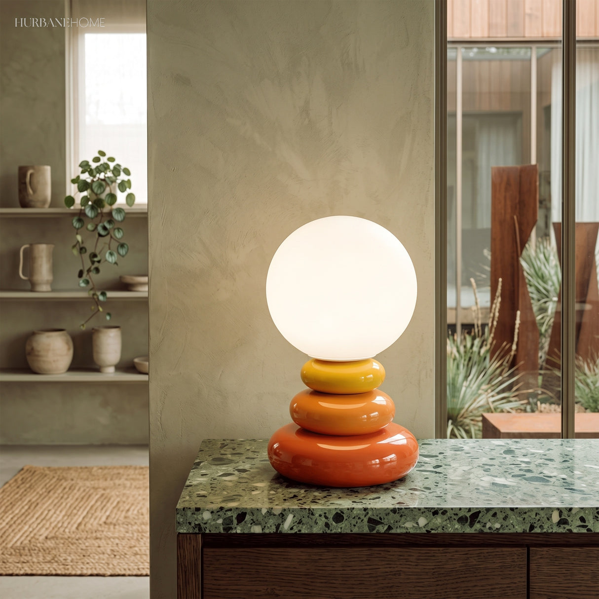 Stacked ceramic lamp lit on a green marble counter in front of a window