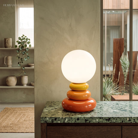 Stacked ceramic lamp lit on a green marble counter in front of a window
