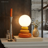 Orange pebble lamp lit beside a candlestick and vase on a pale mantelpiece