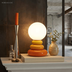 Orange pebble lamp lit beside a candlestick and vase on a pale mantelpiece