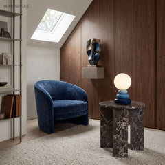 Blue stacked ceramic lamp on a dark marble side table beside a velvet chair