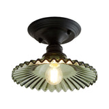 Green ribbed scalloped ceiling light lit warm on a plain background