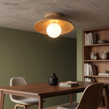 Wood ceiling light lit above a dining table on a green wall