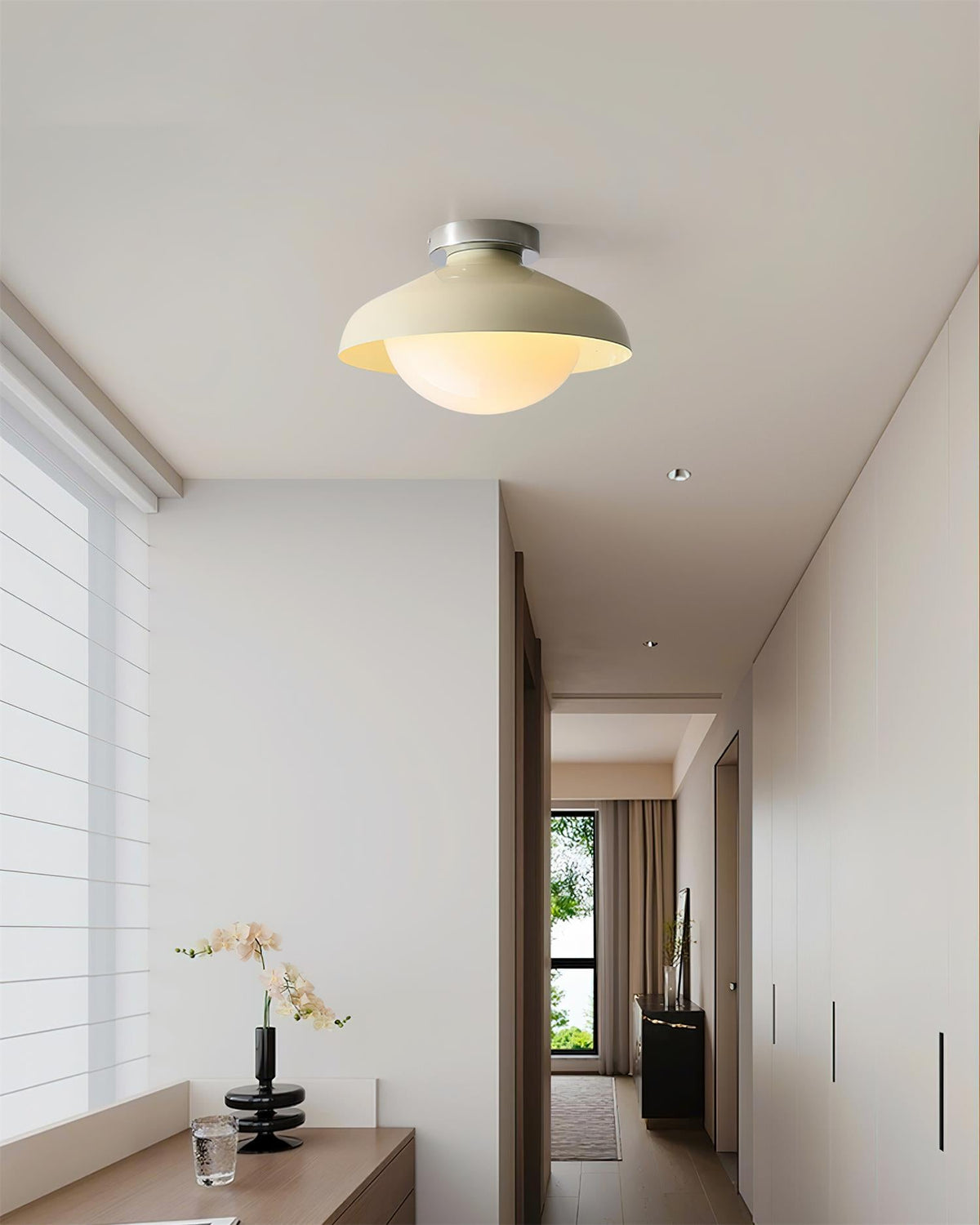 Beige dome ceiling light in a white hallway above an orchid and cabinets