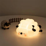 Sheep shaped silicone night light glowing softly beside a small toy sheep