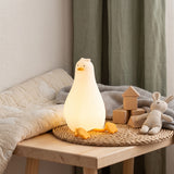 Goose shaped silicone night light glowing warm white on a wooden nursery bench