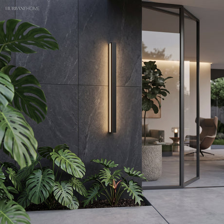 Tall linear wall light on dark stone beside foliage and a glazed living room