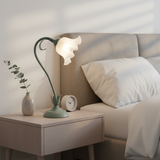 Small flower table lamp lit on a pale nightstand with eucalyptus in a vase