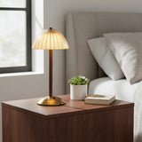 A table lamp with a warm glowing pleated dome shade, a slender matching stem, and a round base, shown against a plain white background.