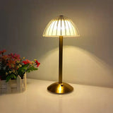 Gold table lamp with a textured glass shade on a white surface, next to a small plant.