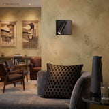 Black square switched sconce on textured wall above a grey sofa
