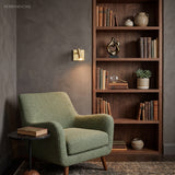 Brass square switched sconce beside a bookcase and green armchair