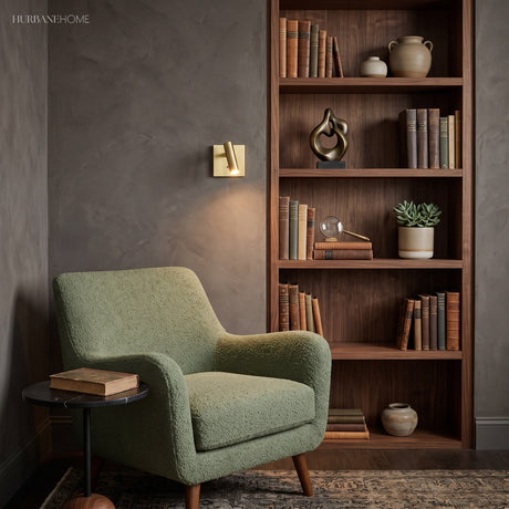 Brass square switched sconce beside a bookcase and green armchair