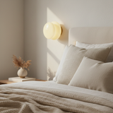 Soft yellow glass wall sconce lighting a corner above a made bed