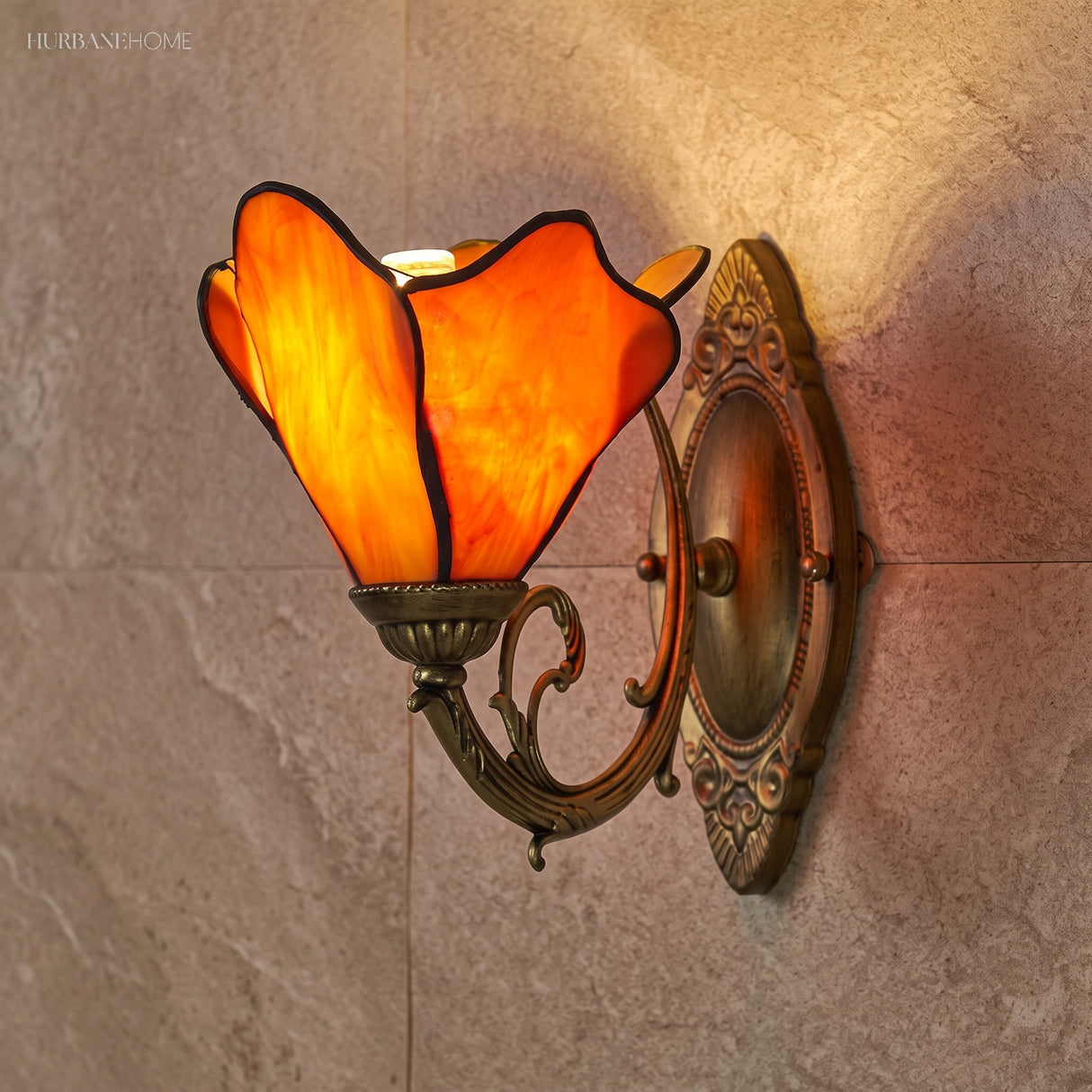 Amber stained glass petal sconce lit against a stone tiled wall