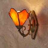 Amber stained glass petal sconce lit against a stone tiled wall