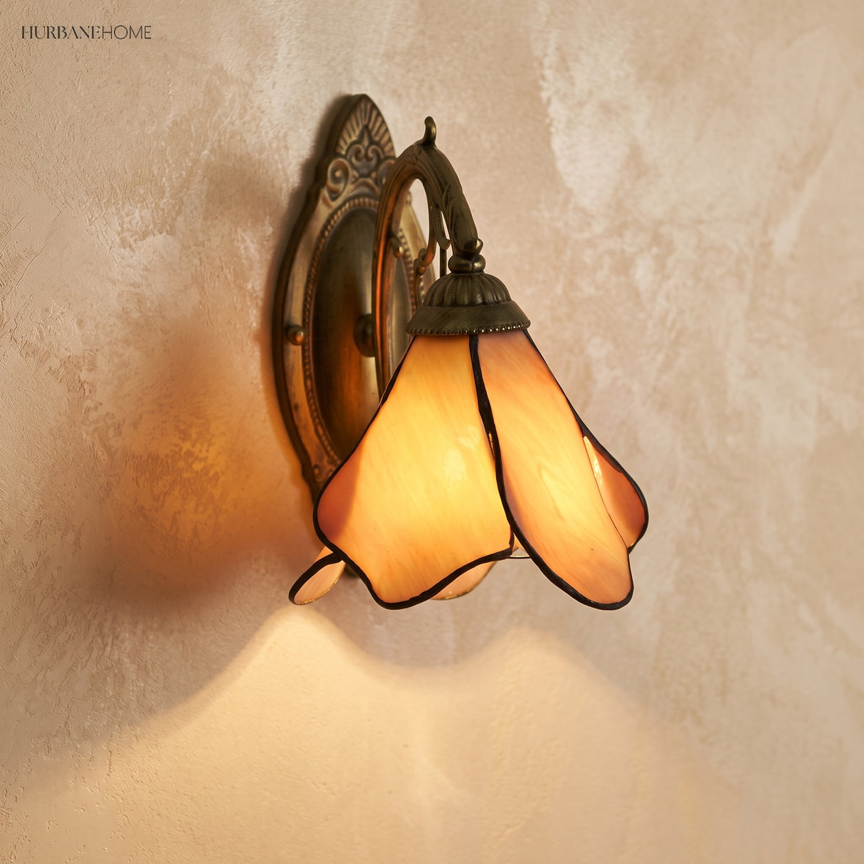 Cream and peach glass petal sconce casting a warm downward glow on plaster