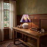 Leaded glass lamp lighting a dark panelled dining room with stacked books