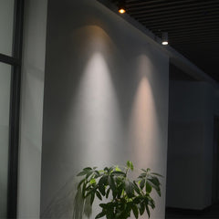 Two cylinder ceiling lights washing warm light down a grey wall